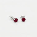 Pair of oval deep red gemstone stud earrings in sterling silver four prong settings on a white background.