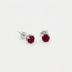Pair of oval deep red gemstone stud earrings in sterling silver four prong settings on a white background.
