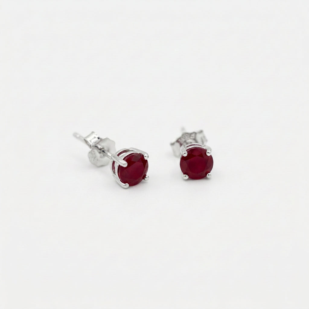 Pair of oval deep red gemstone stud earrings in sterling silver four prong settings on a white background.