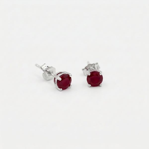 Pair of oval deep red gemstone stud earrings in sterling silver four prong settings on a white background.
