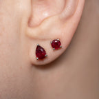 A close-up of a person's ear wearing two red gemstone stud earrings in silver settings.