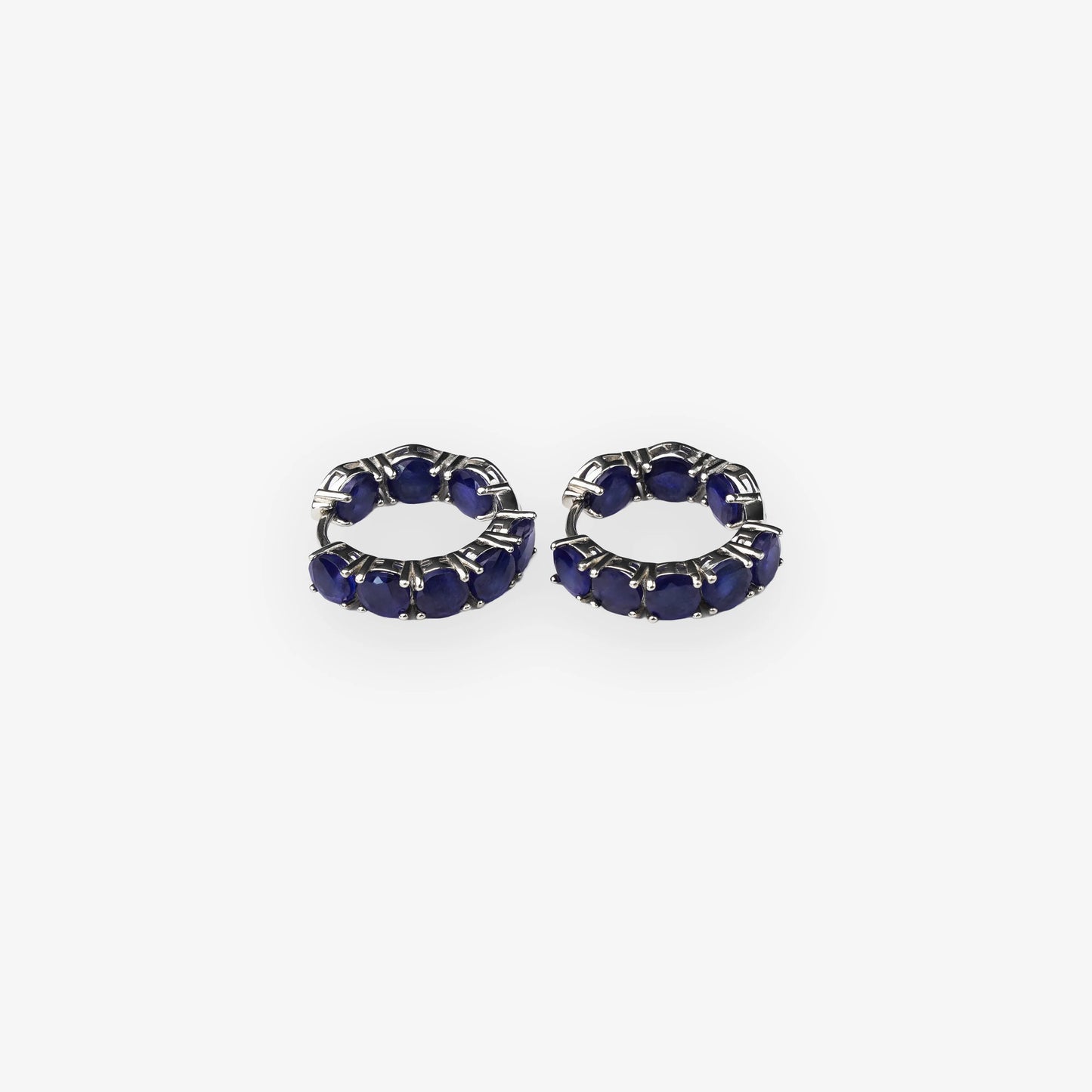 A pair of small silver hoop earrings set with deep blue sapphire oval gemstones, shown on a plain light grey background.
