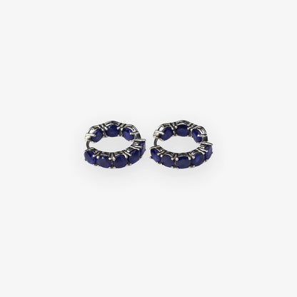 A pair of small silver hoop earrings set with deep blue sapphire oval gemstones, shown on a plain light grey background.