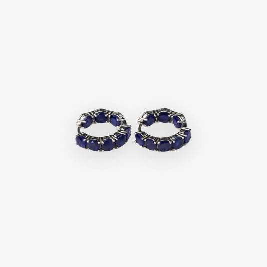A pair of small silver hoop earrings set with deep blue sapphire oval gemstones, shown on a plain light grey background.