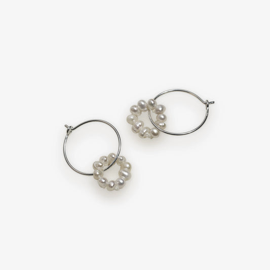 silver wire hoop dangled with pearl on a off white background.