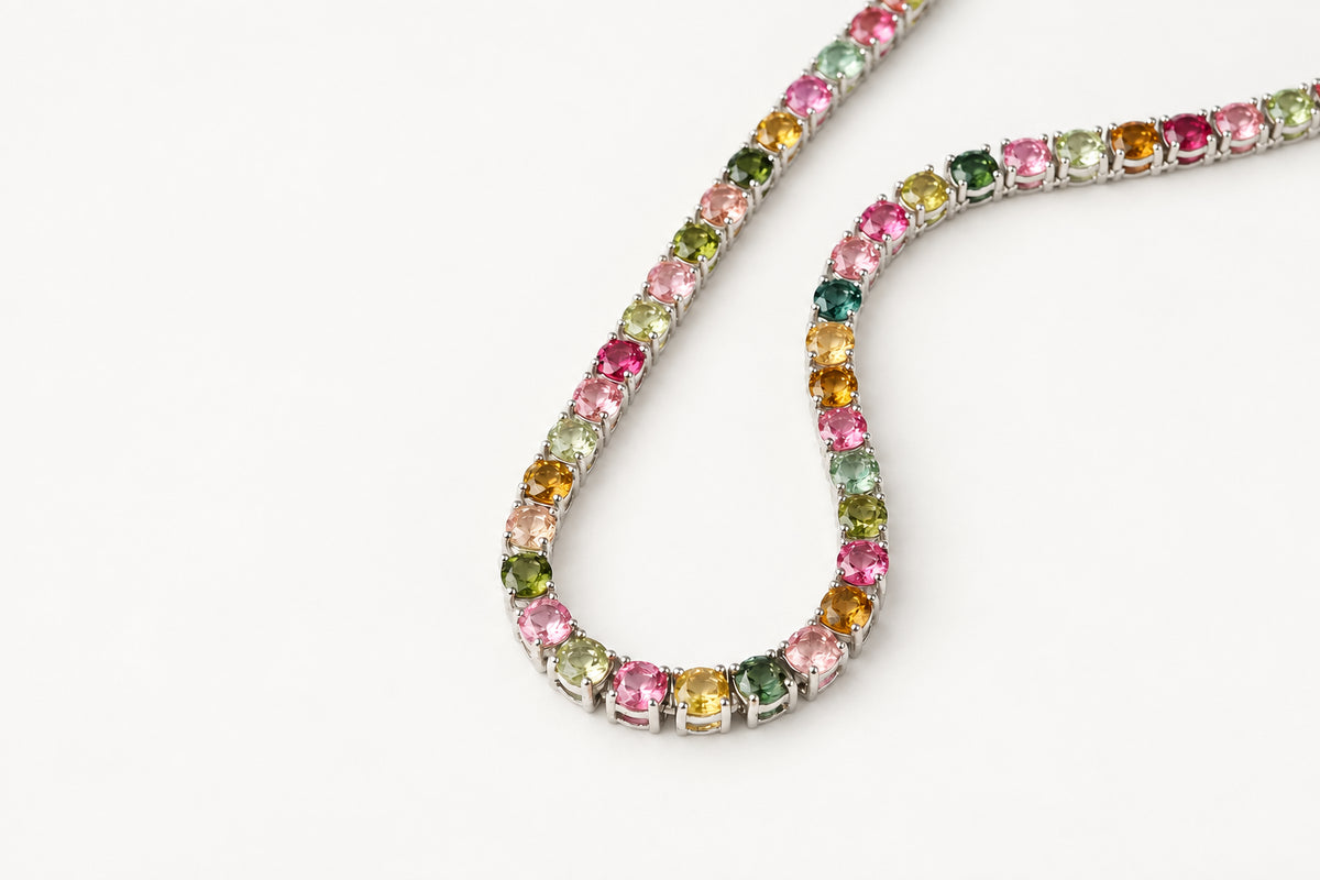 A silver tennis necklace featuring a continuous row of colorful round-cut gemstones in pink, green, yellow, and orange, displayed on a clean white background.