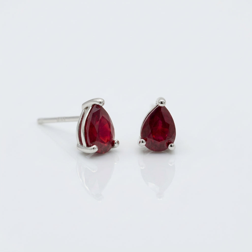 A pair of gold oval stud earrings with smooth, polished red cabochon gemstones, set against a solid white background.
