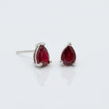 A pair of gold oval stud earrings with smooth, polished red cabochon gemstones, set against a solid white background.
