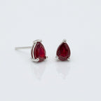 A pair of gold oval stud earrings with smooth, polished red cabochon gemstones, set against a solid white background.