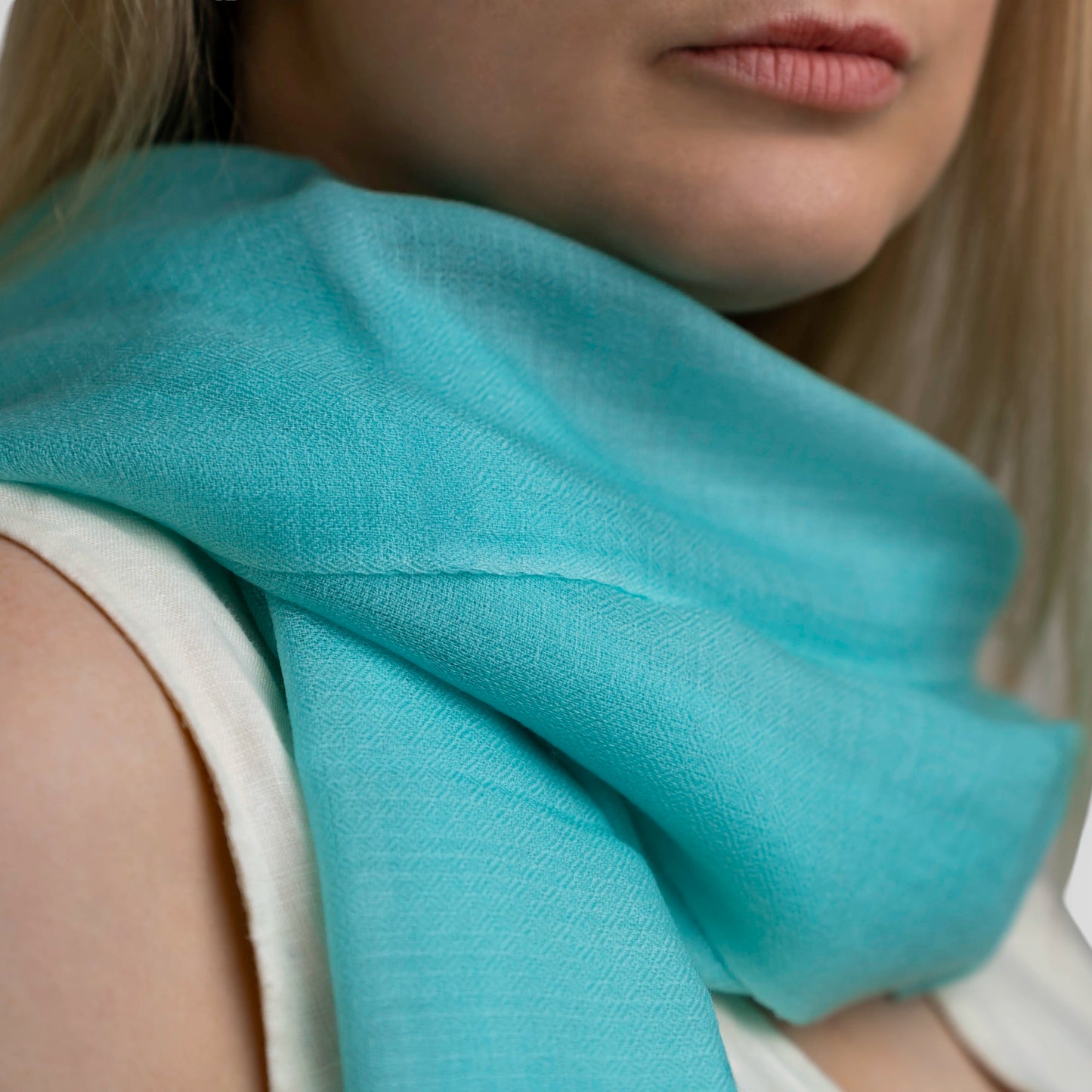 A close-up of a woman wearing a soft, lightweight turquoise scarf draped around her neck over a white top.