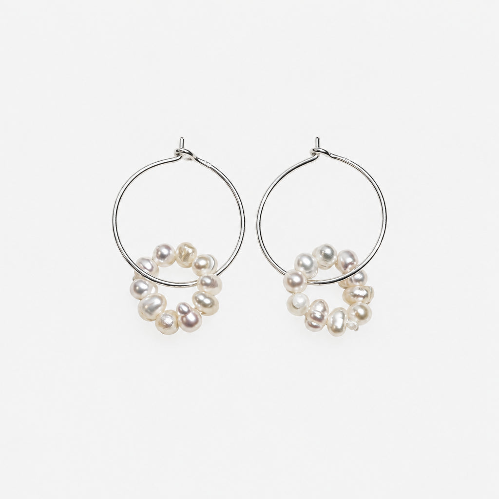 silver wire hoop dangled with pearl on a off white background.