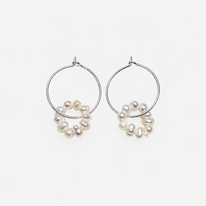 silver wire hoop dangled with pearl on a off white background.