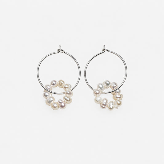 silver wire hoop dangled with pearl on a off white background.