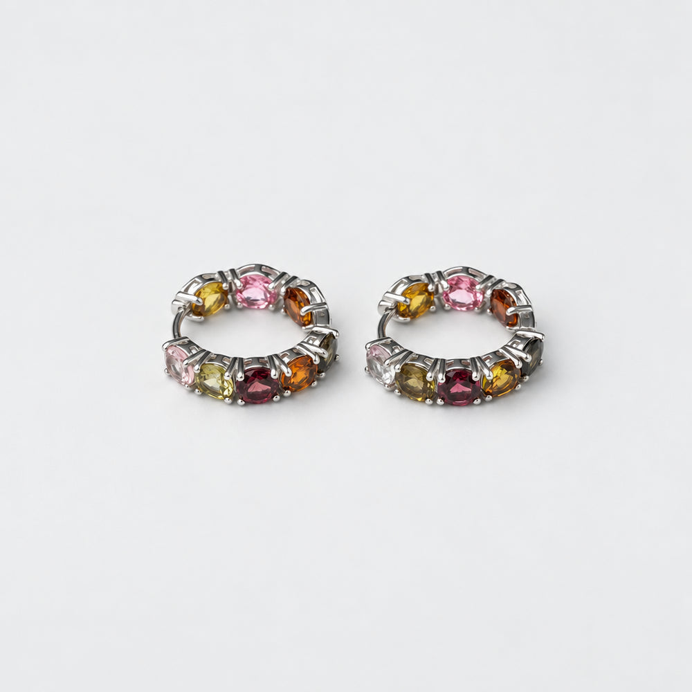 A pair of silver-toned huggie hoop earrings set with multiple small round tourmaline gemstones in pink, yellow, green, and purple hues, displayed on a clean white background.
