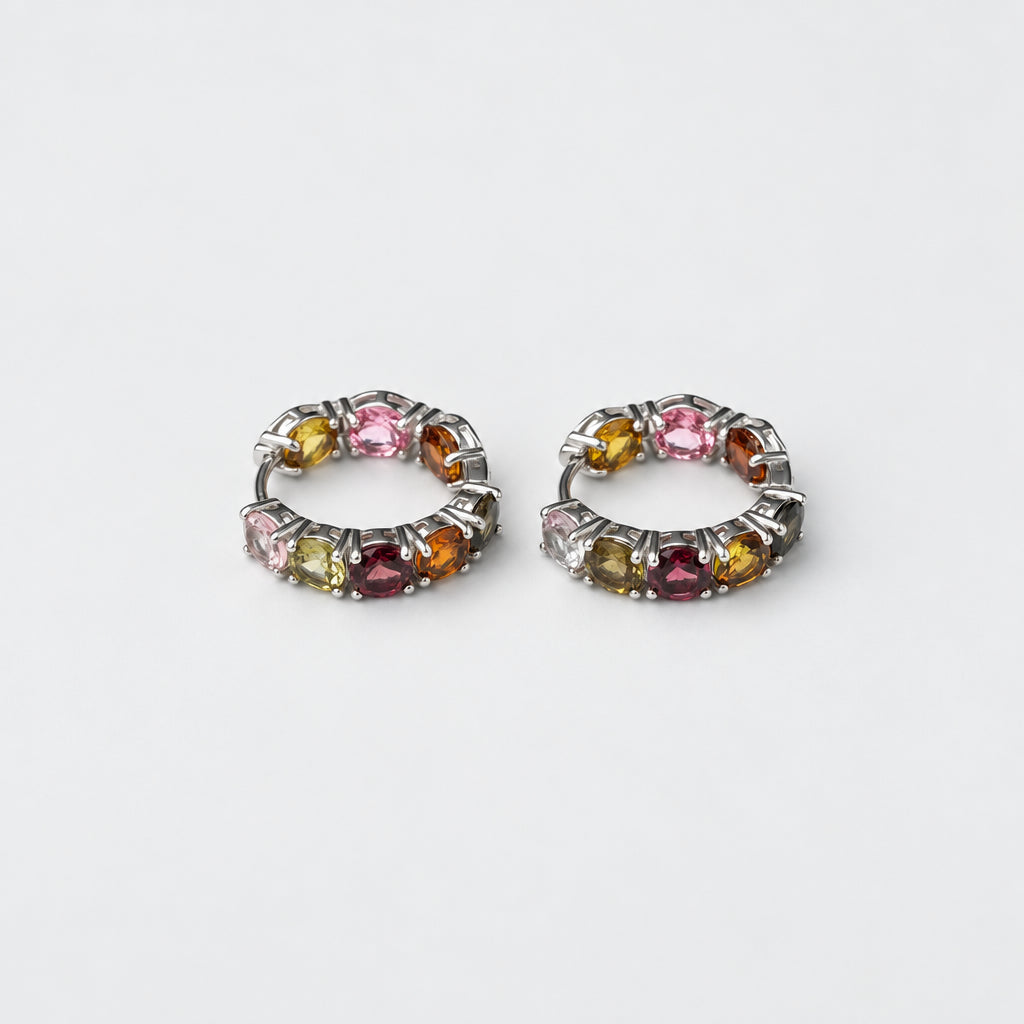 A pair of silver-toned huggie hoop earrings set with multiple small round tourmaline gemstones in pink, yellow, green, and purple hues, displayed on a clean white background.