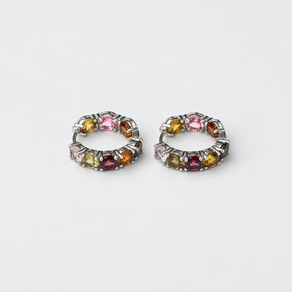 A pair of silver-toned huggie hoop earrings set with multiple small round tourmaline gemstones in pink, yellow, green, and purple hues, displayed on a clean white background.
