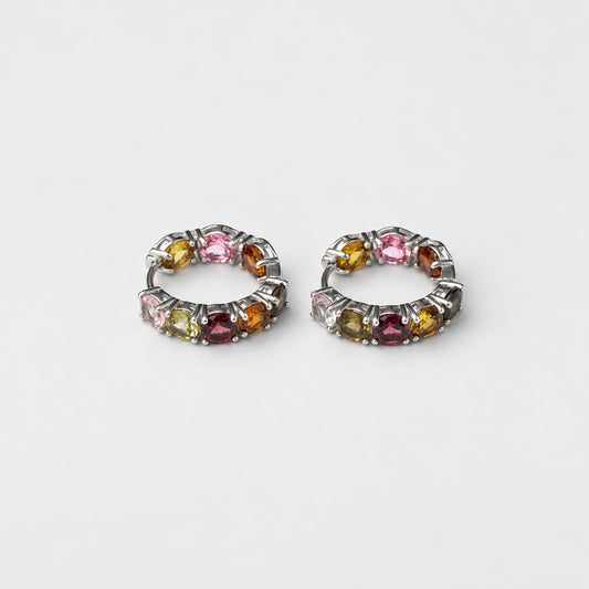 A pair of silver-toned huggie hoop earrings set with multiple small round tourmaline gemstones in pink, yellow, green, and purple hues, displayed on a clean white background.